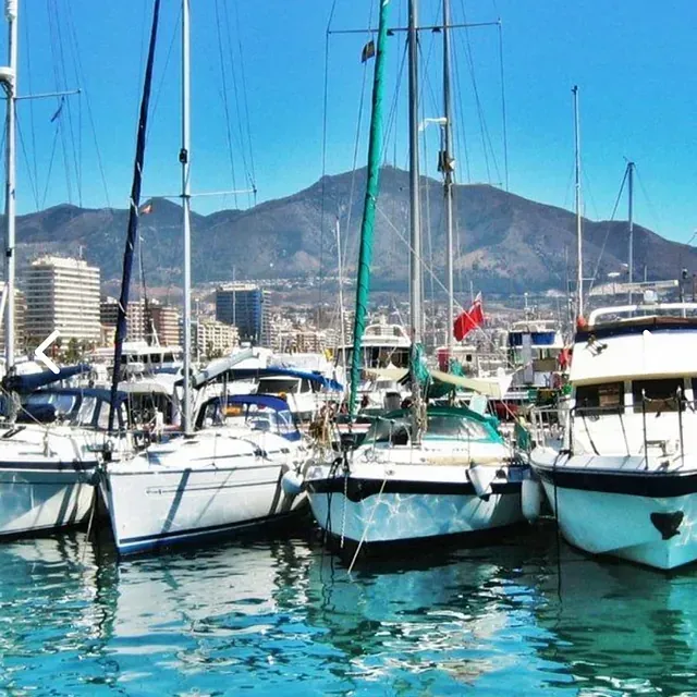 Varios barcos están atracados en un puerto con montañas al fondo.