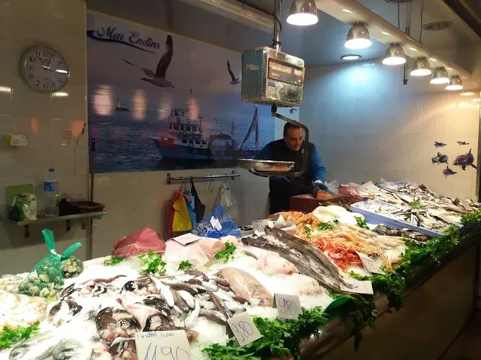 Un hombre está parado frente a una exhibición de pescado en un mercado de pescado.
