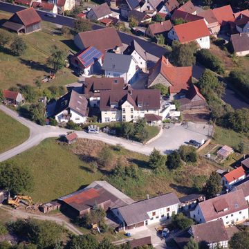 Koch hält Holzlöffel in Pfanne, streut Pfeffer mit der anderen