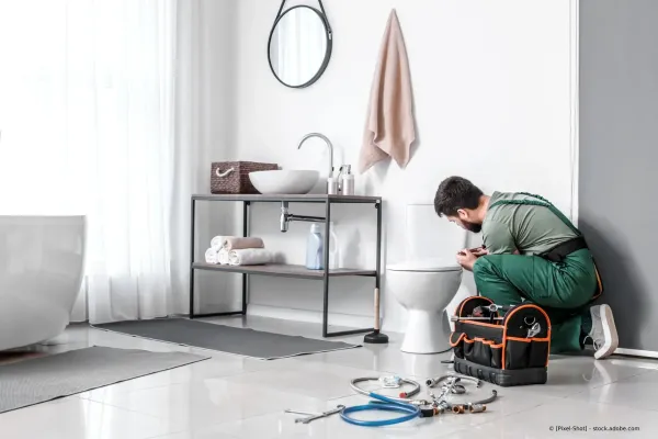 Ein Techniker kniet neben einem Waschbecken im Badezimmer und repariert ein Leck mit Werkzeugen auf dem Boden.