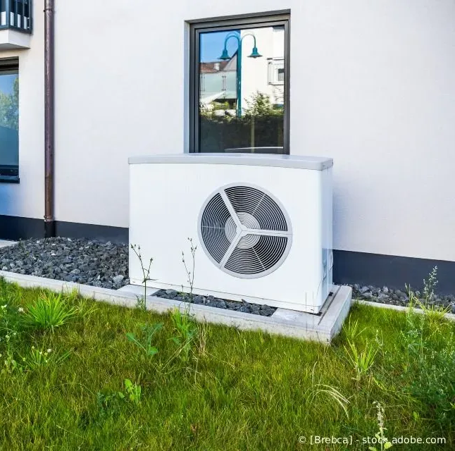 Zwei weiße Außenklimaanlagen neben einem Haus auf einem Rasen