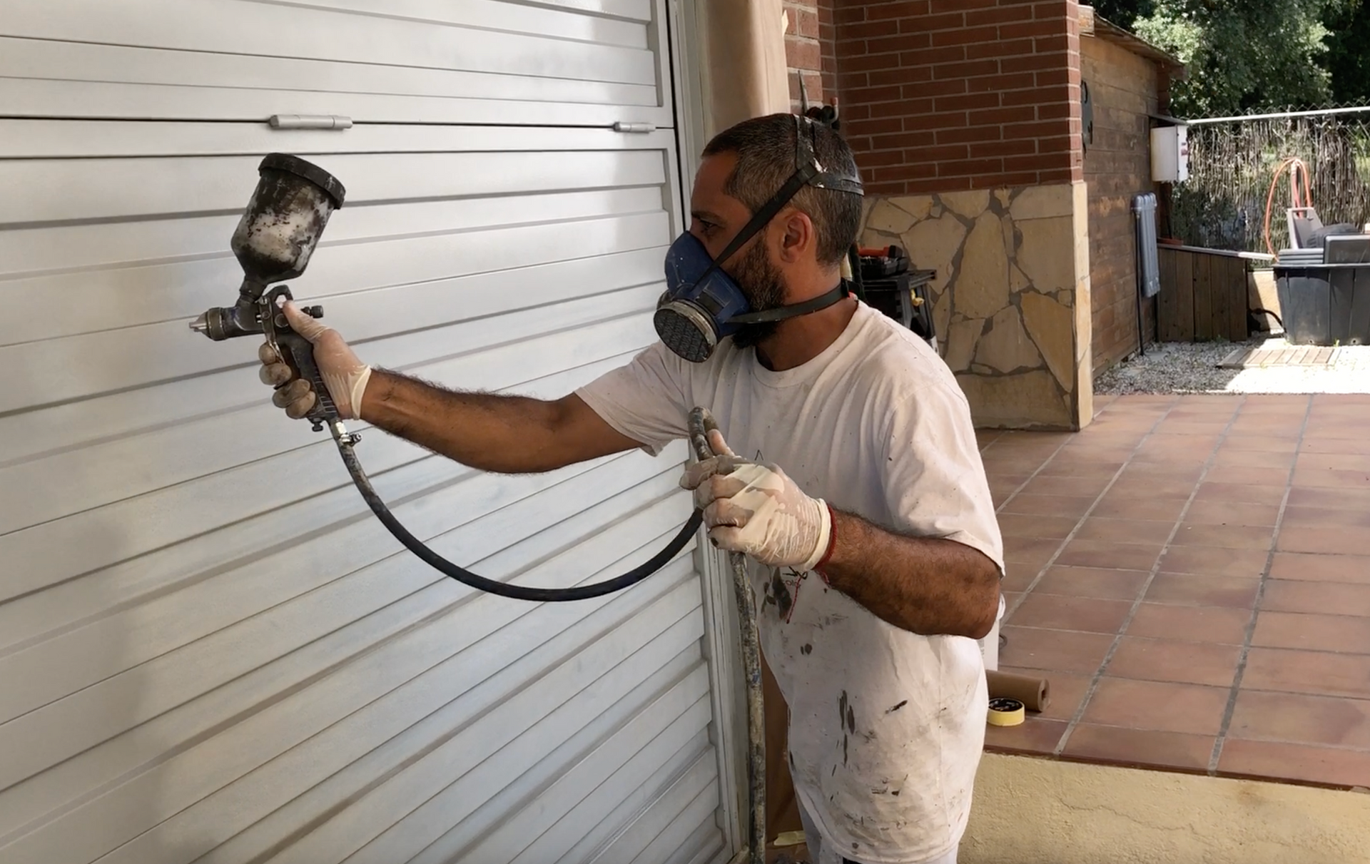 Un hombre que lleva una máscara está pintando con aerosol una puerta de garaje.