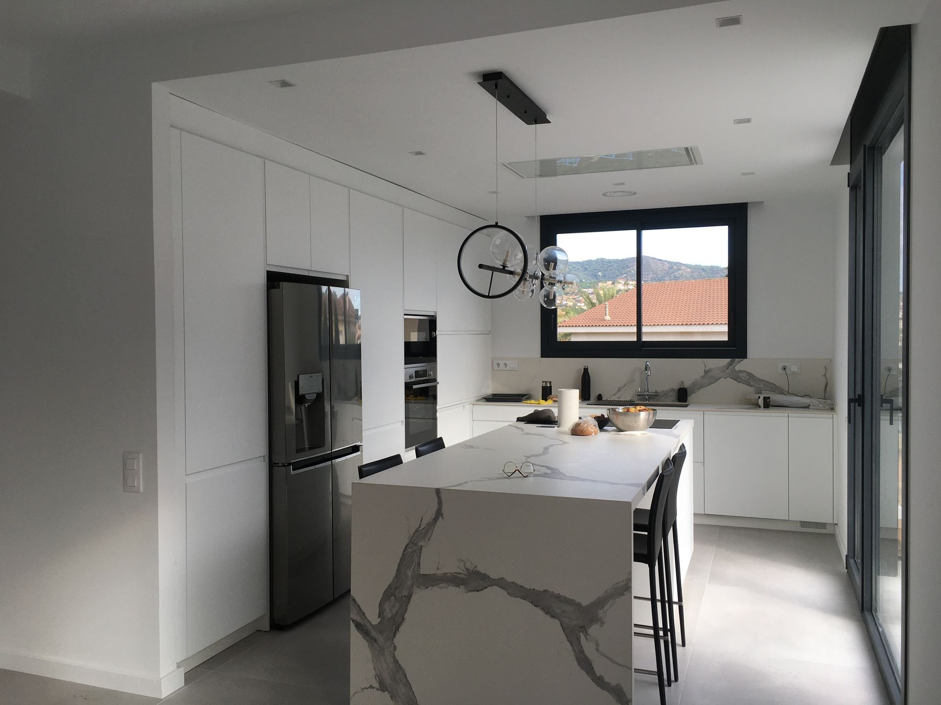 Una cocina con gabinetes blancos, una gran isla, un refrigerador y un reloj colgando del techo.