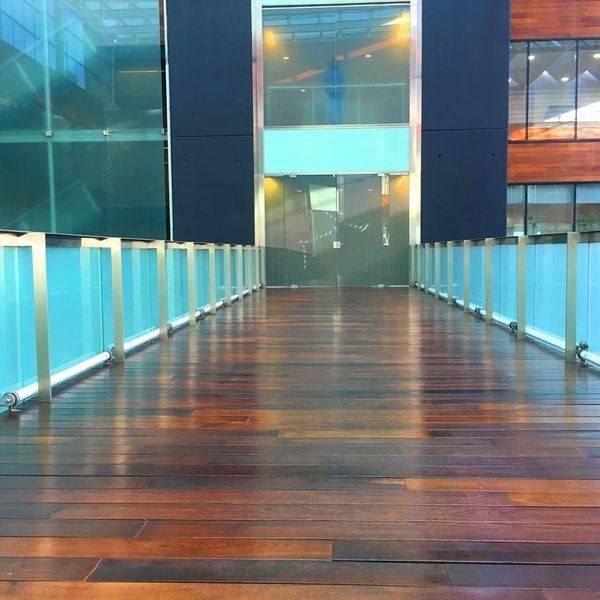 Una pasarela de madera que conduce a un edificio con barandilla de vidrio.