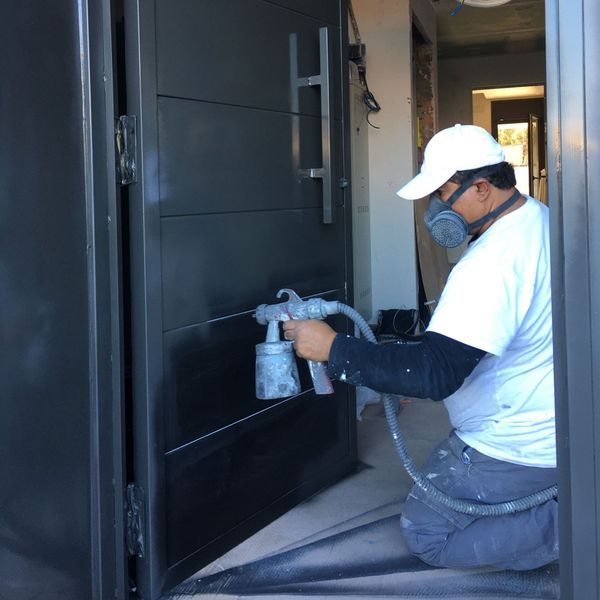 Un hombre con una máscara está rociando pintura en una puerta.