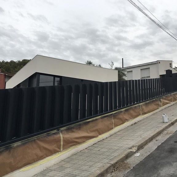 Una valla negra rodea una casa blanca en una colina.