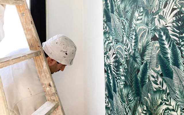 Un hombre está de pie en una escalera mirando una pared.