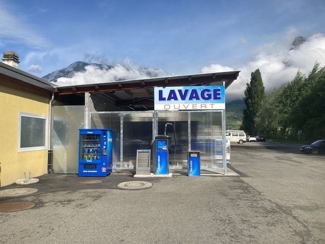 Station de lavage auto en libre-service avec distributeurs automatiques bleus et une grande enseigne « LAVAGE »