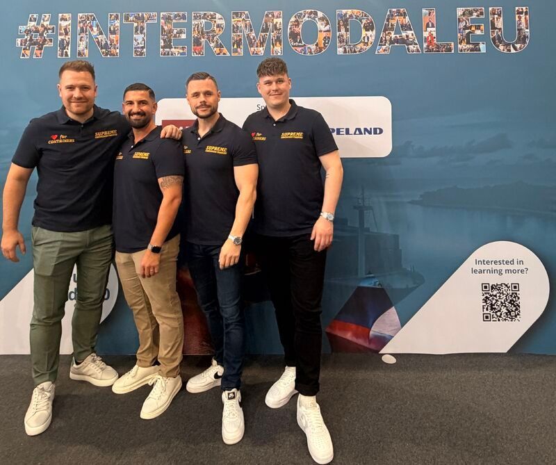 Vier Männer in dunkelblauen Hemden posieren vor einem Banner bei einer Veranstaltung von Intermodal EU.