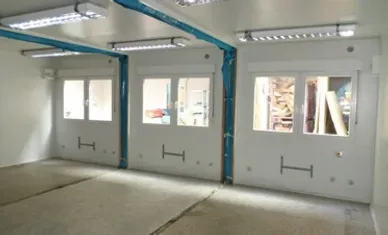 Innenansicht eines weißen Raumes mit drei Fenstern, Leuchtstoffröhren und blauen Leitungen.