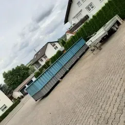 Ein langer, rechteckiger, blau-grauer Container auf einem Anhänger, der auf einer gepflasterten Auffahrt parkt