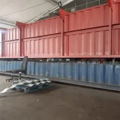 Rote und blaue Industrieanlagen in einer Lagerhalle, daneben ein Stuhl und eine Palette.