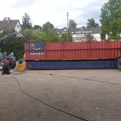 Ein Schweißer arbeitet auf einem Parkplatz an einem großen blau-roten Schiffscontainer.