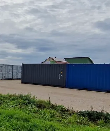 Bunte Lagerbehälter unter bewölktem Himmel. Grünes Gras im Vordergrund.