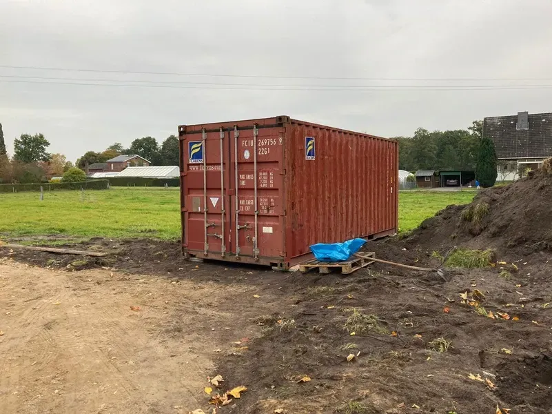 Ein roter Schiffscontainer auf einer Palette in einem matschigen Feld. Ländliche Umgebung mit Grünflächen