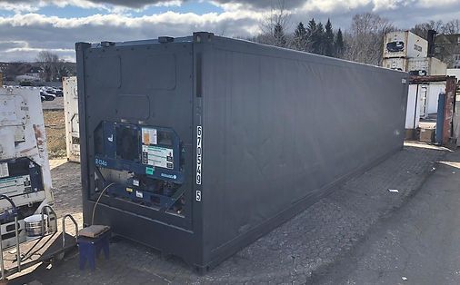 Dunkelgrauer Kühlcontainer auf einer Kiesfläche im Freien.