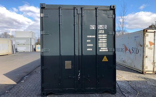 Dunkelgrüner Versandcontainer mit weißer Schrift und gelbem Gefahrensymbol, im Freien.