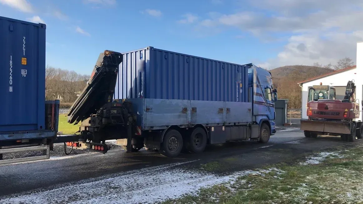 Ein LKW mit einem blauen Schiffscontainer und einem Kran
