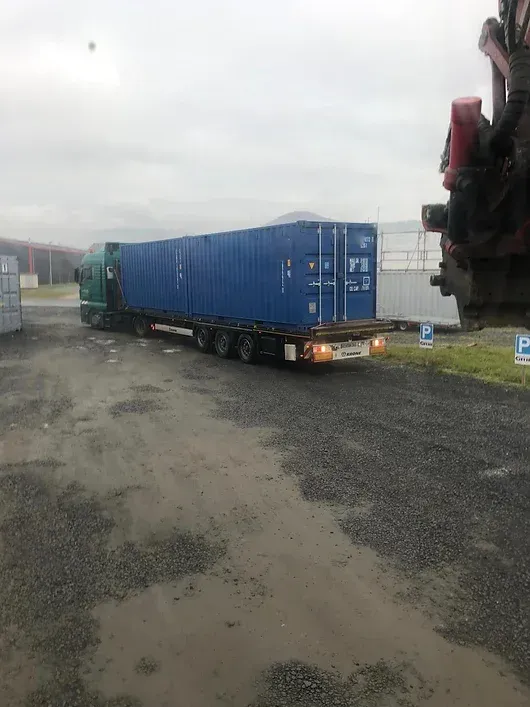 Blauer Schiffscontainer auf einem Pritschenwagen in einem Industriegebiet, bereit zum Transport.