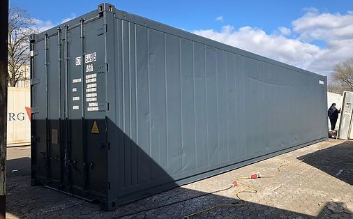 Grauer Schiffscontainer auf Kies, eine Person in der Nähe.