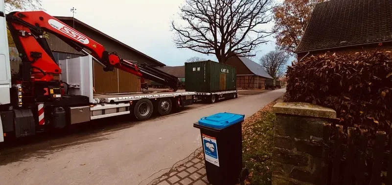 Ein Lastwagen mit Kran transportiert einen grünen Container auf einem Anhänger eine Straße