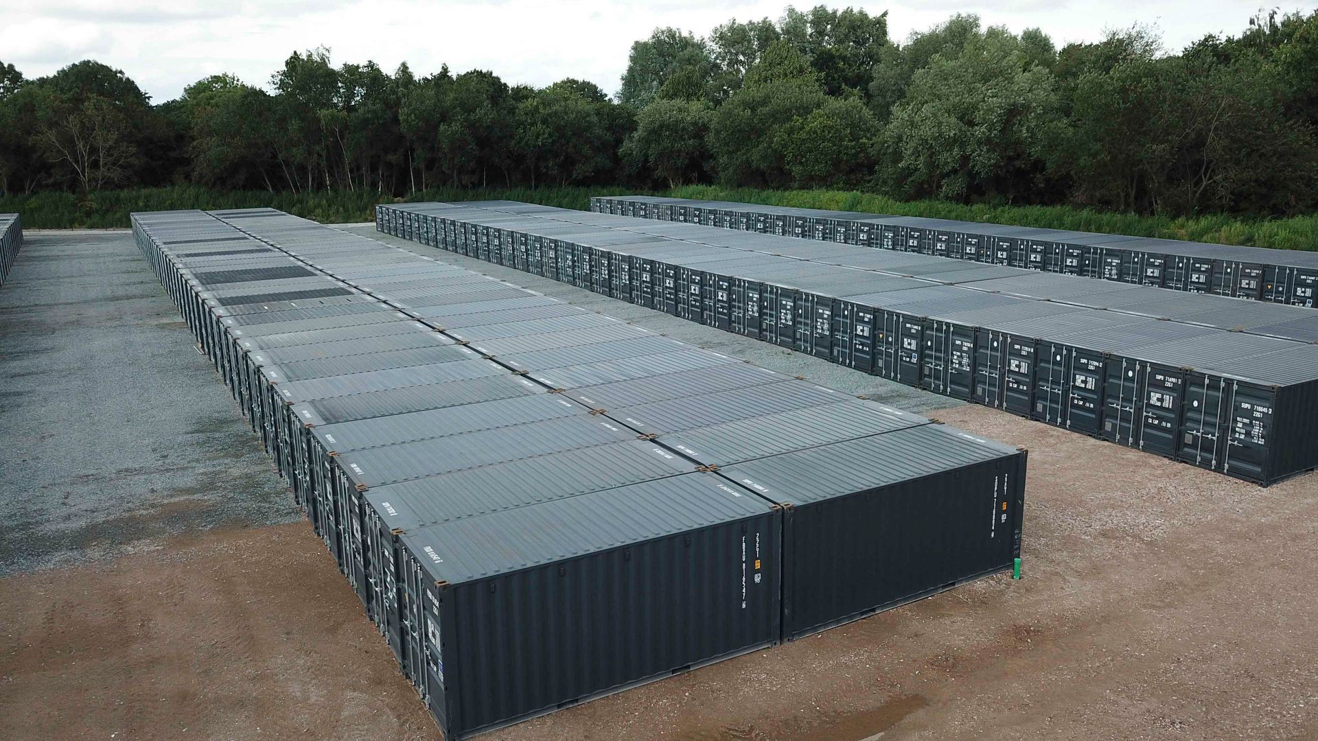 Reihen von rechteckigen grauen Lagercontainern in einer Freiluftlagerhalle.