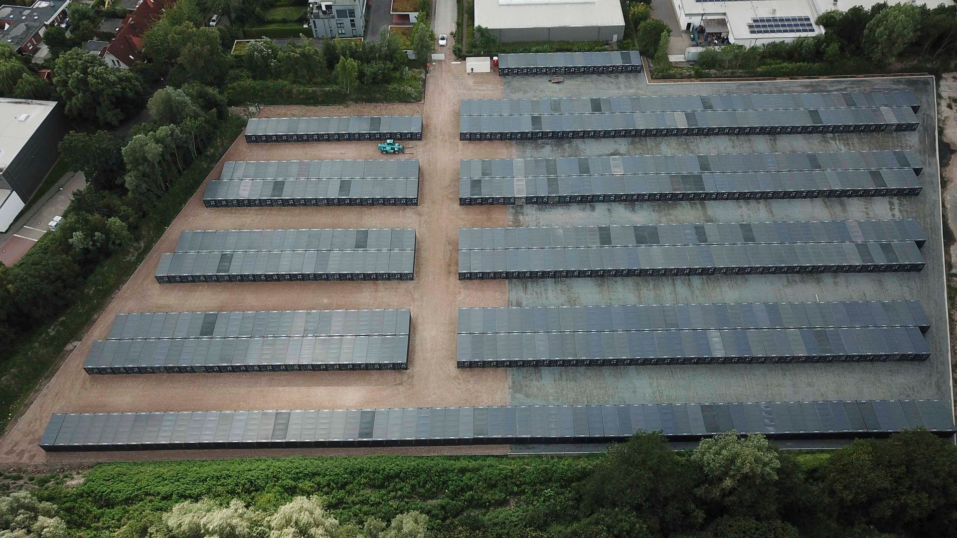 Luftaufnahme eines Parkplatzes mit langen, rechteckigen Gebäuden; Bäume säumen den unteren Rand