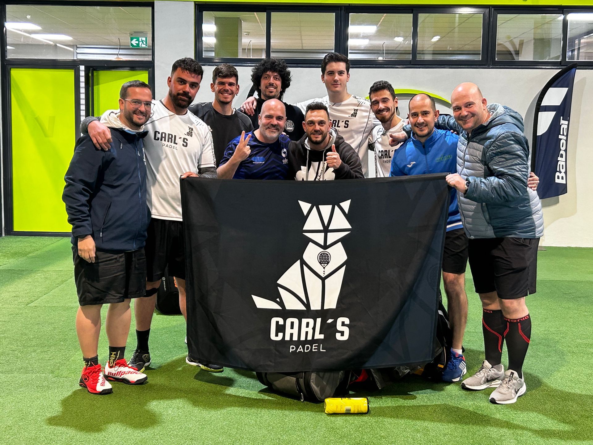 Un grupo de hombres posa para una foto con una bandera de Carl's Padel.