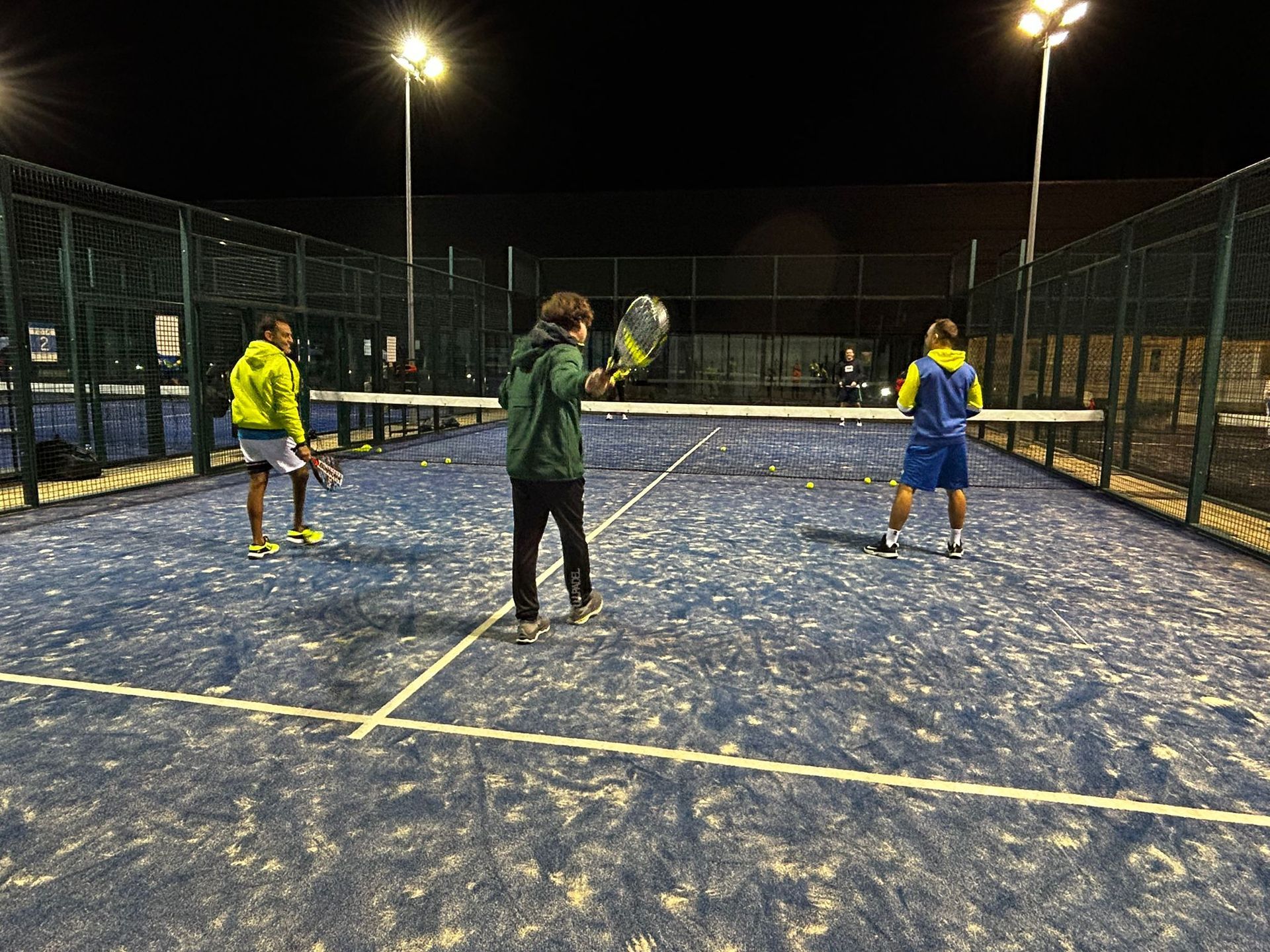 Un grupo de personas está jugando al tenis en una cancha por la noche.