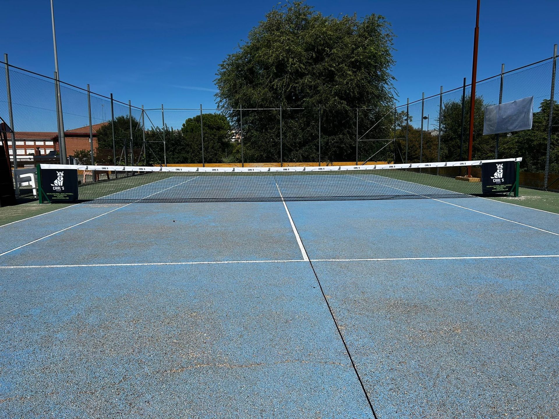 Una cancha de tenis con una red y algunos árboles al fondo.