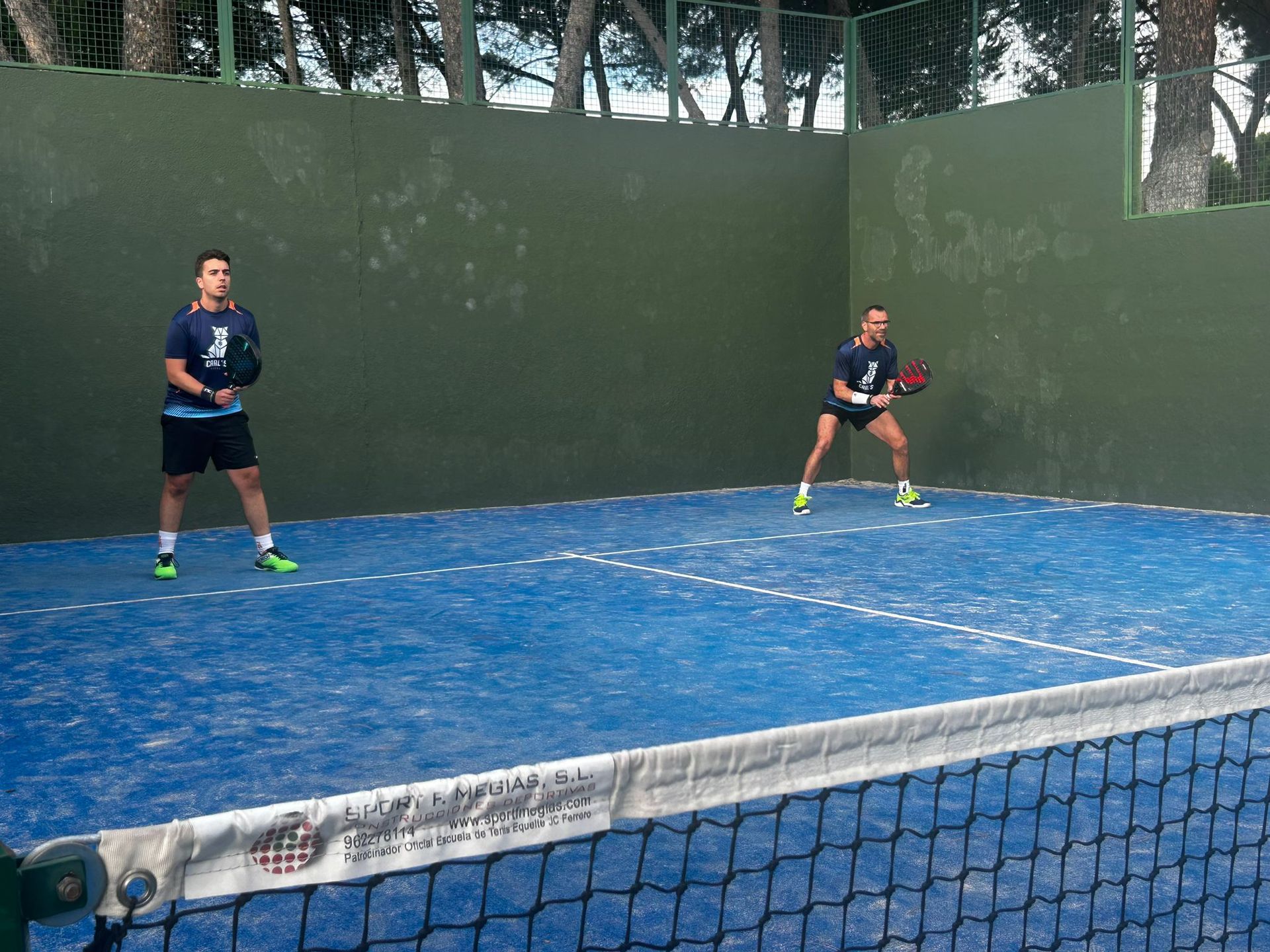 Dos personas están jugando al tenis en una cancha azul.