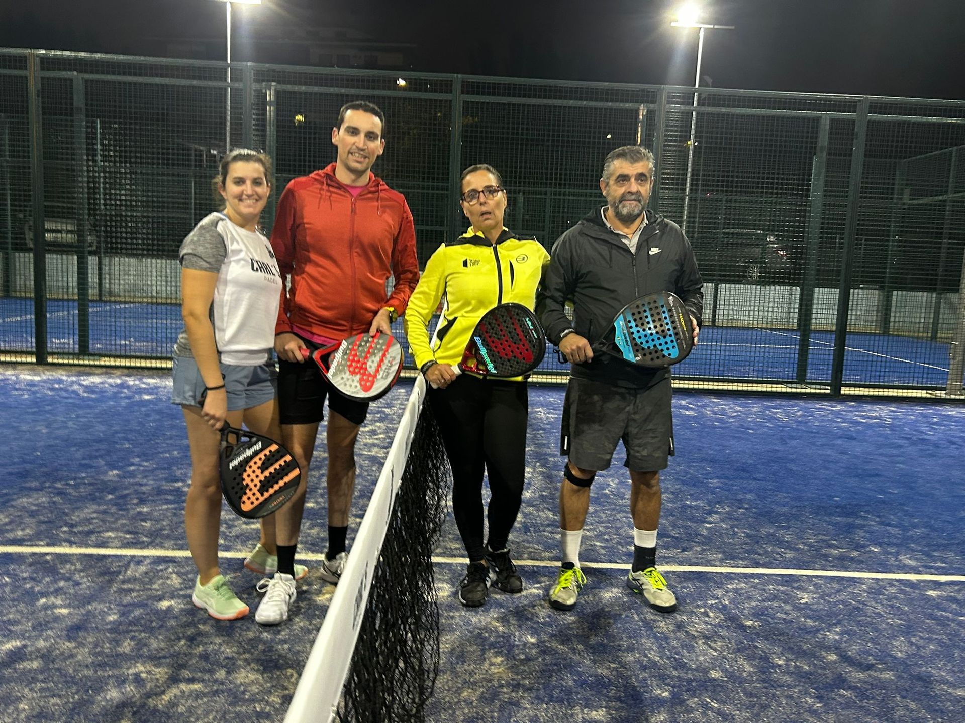 Un grupo de personas están de pie una al lado de la otra en una cancha de tenis sosteniendo paletas.