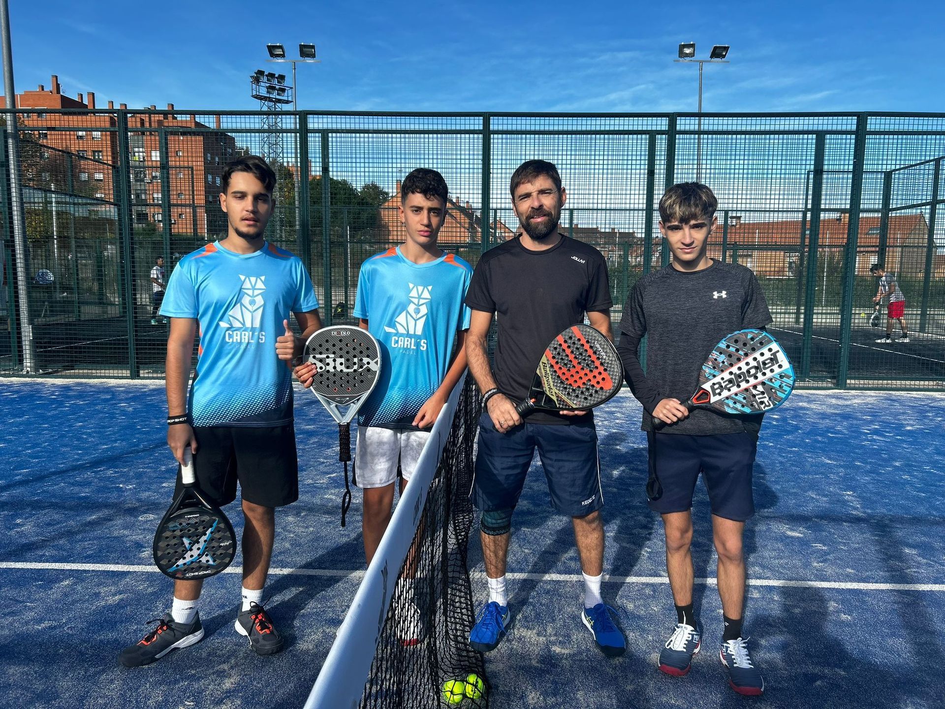 Un grupo de jóvenes están de pie en una cancha de tenis sosteniendo raquetas de tenis.