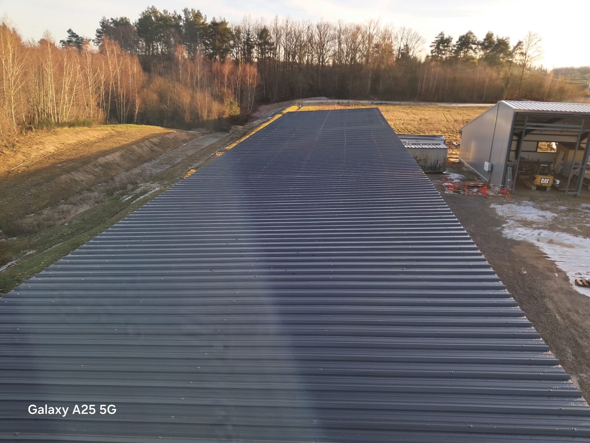 Grange à toit métallique et bardage en bois foncé, avec un toit à pignon et une porte entrouverte.