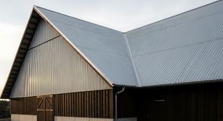 Grange à toit métallique et bardage en bois foncé, avec un toit à pignon et une porte entrouverte.