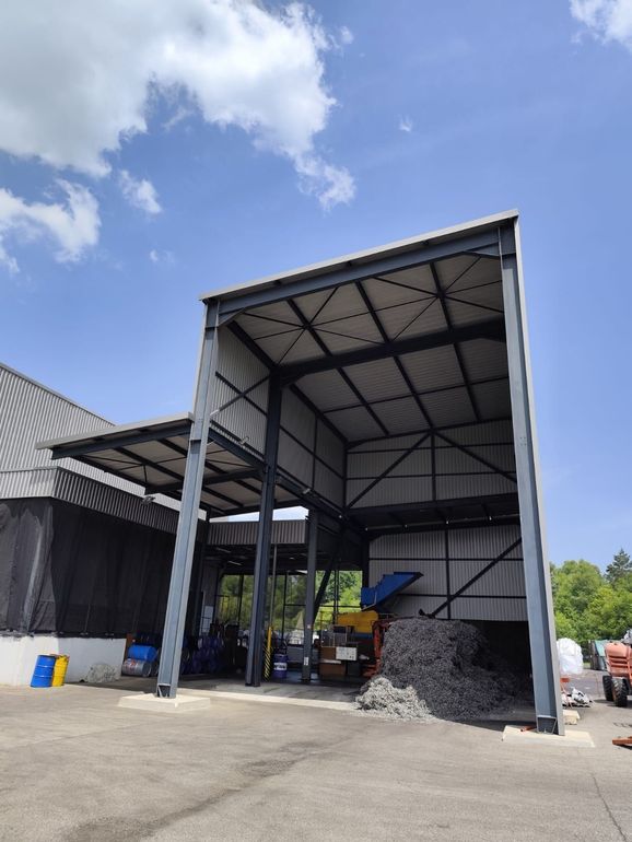 Un hangar à structure métallique avec un grand tas de matériaux.