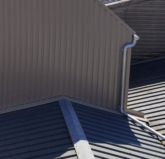 Bâtiment en tôle ondulée brune avec gouttières argentées sur un toit gris.