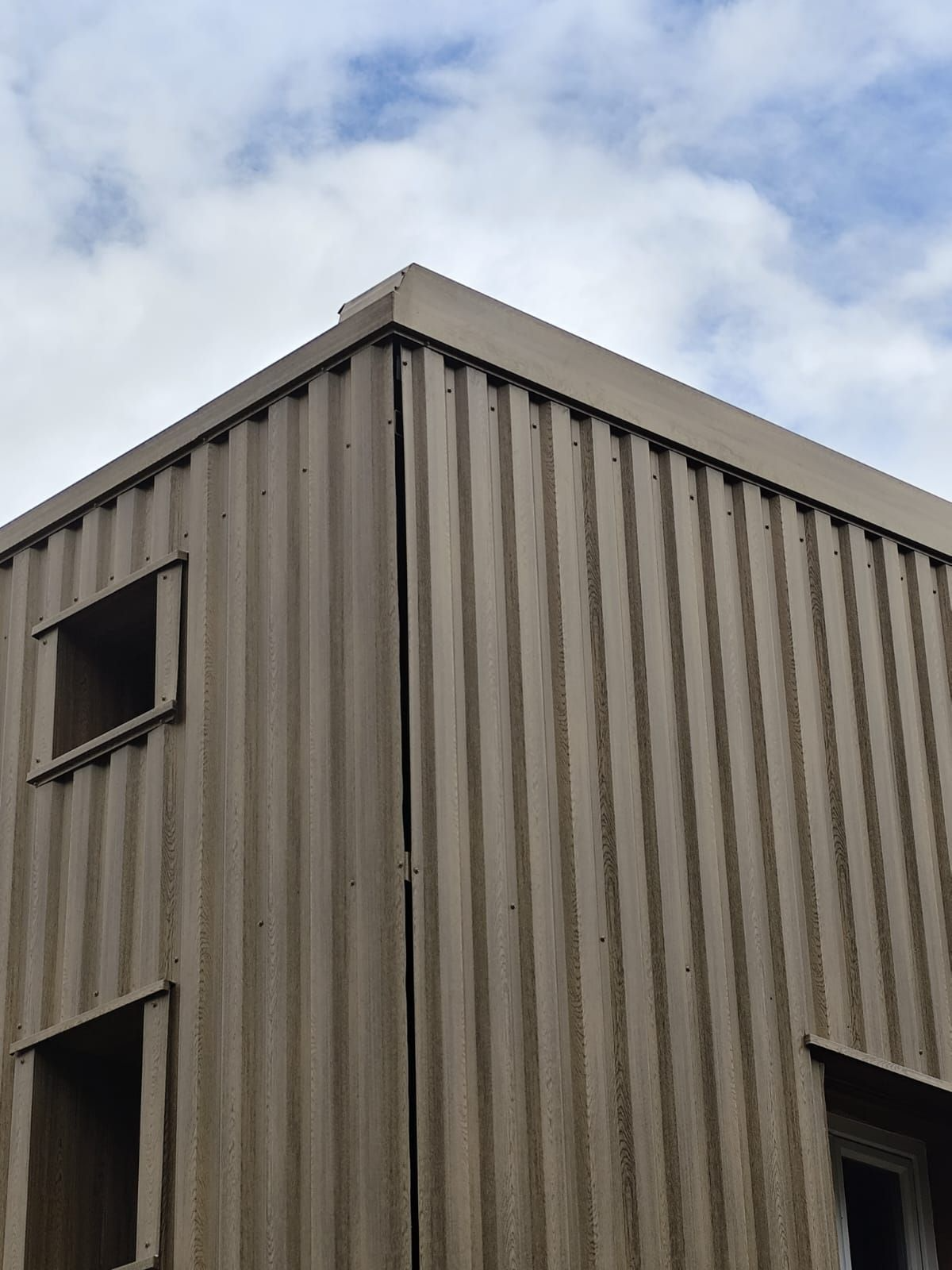 Coin d'un bâtiment en tôle ondulée avec deux ouvertures de fenêtre.