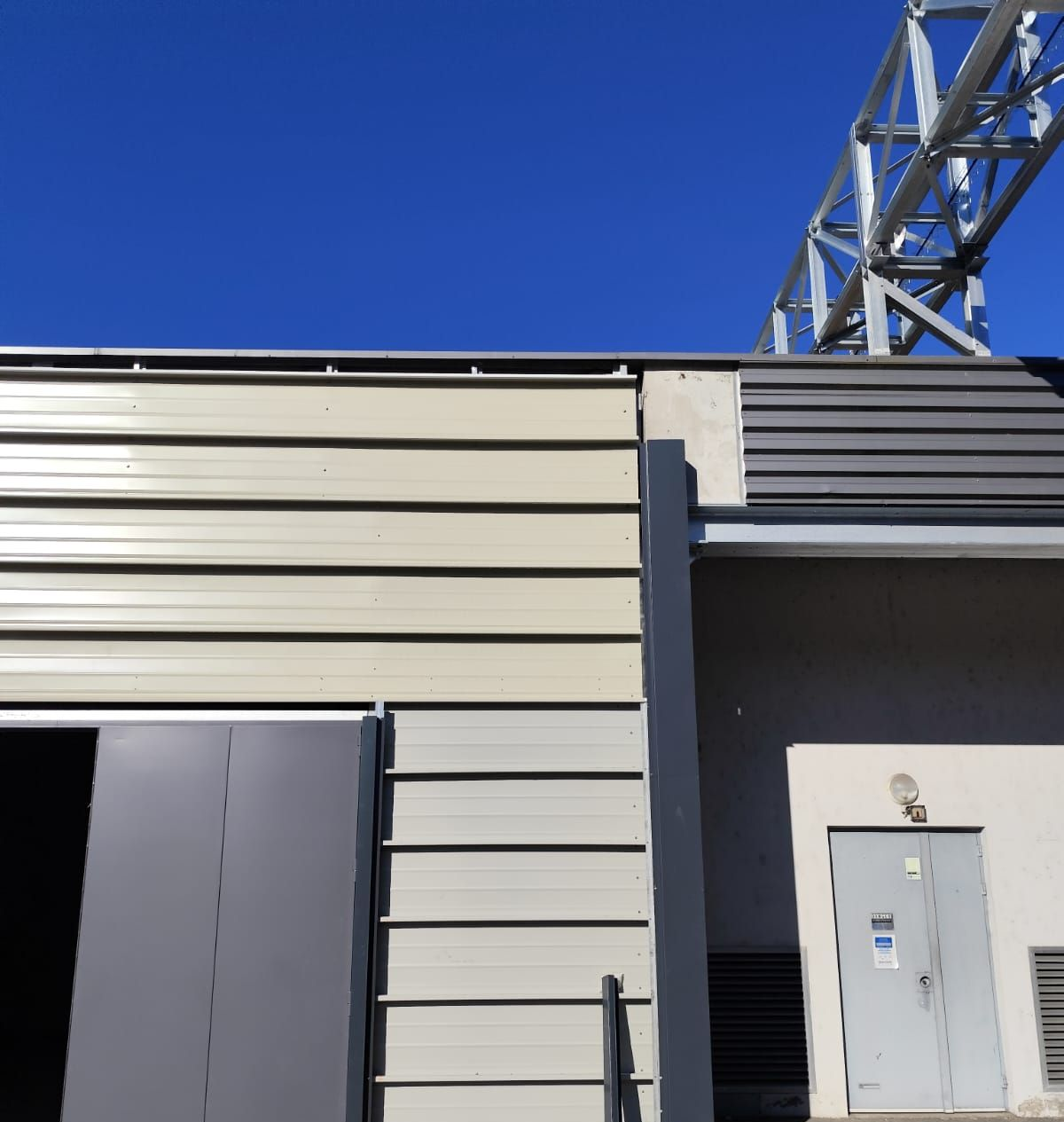 Extérieur d'un bâtiment à bardage horizontal, porte grise et structure métallique.