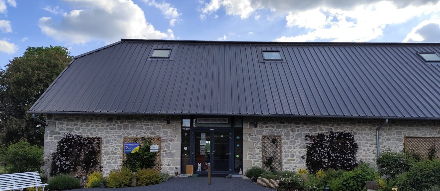 Bâtiment au toit sombre et aux murs de pierre, avec des plantes devant.