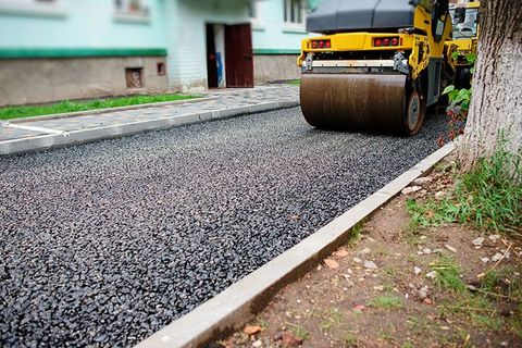 Eine gelbe Walze rollt Asphalt auf eine Straße.