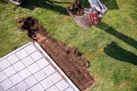 Eine Person gräbt ein Loch ins Gras neben einem Ziegelweg.