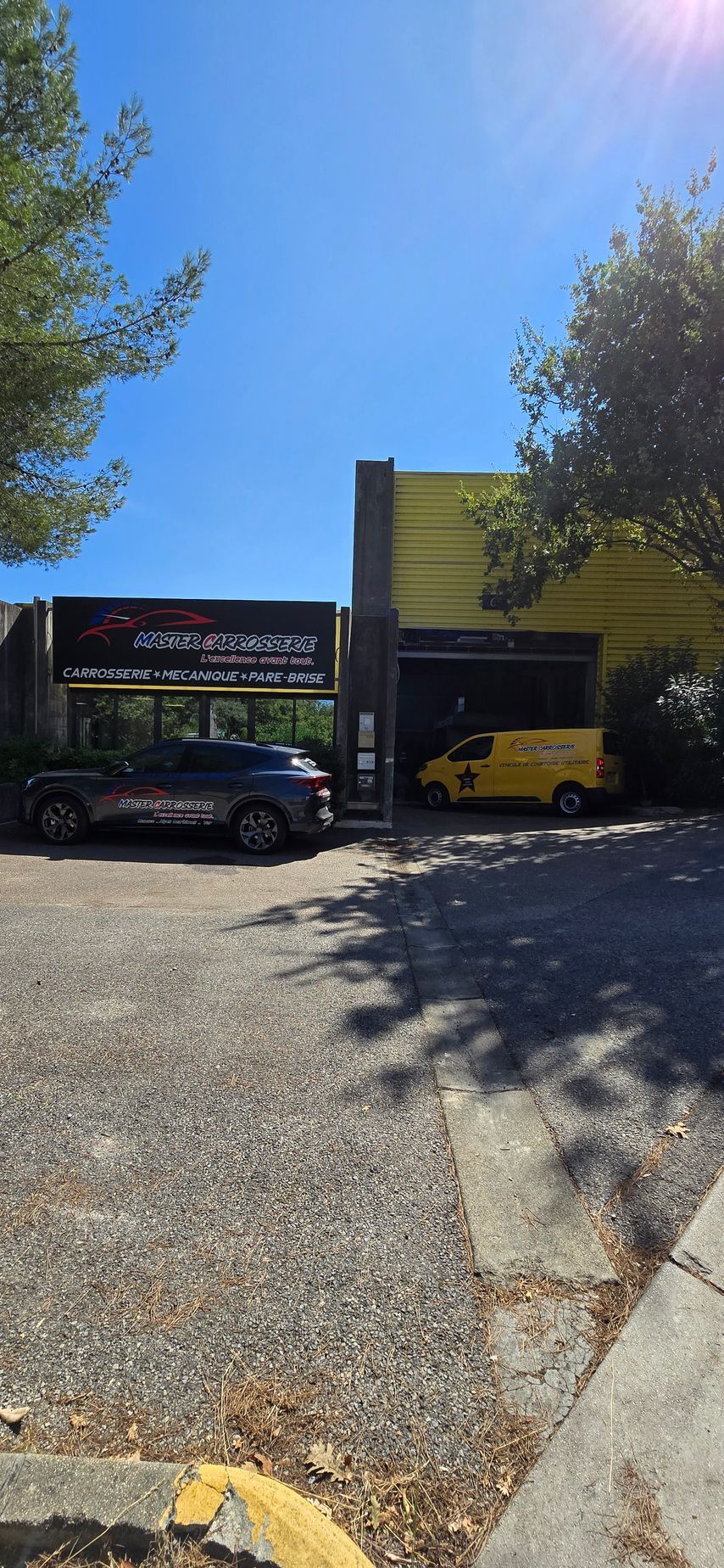 Un bâtiment avec deux véhicules garés à l'extérieur sur une allée de gravier sous un ciel bleu.