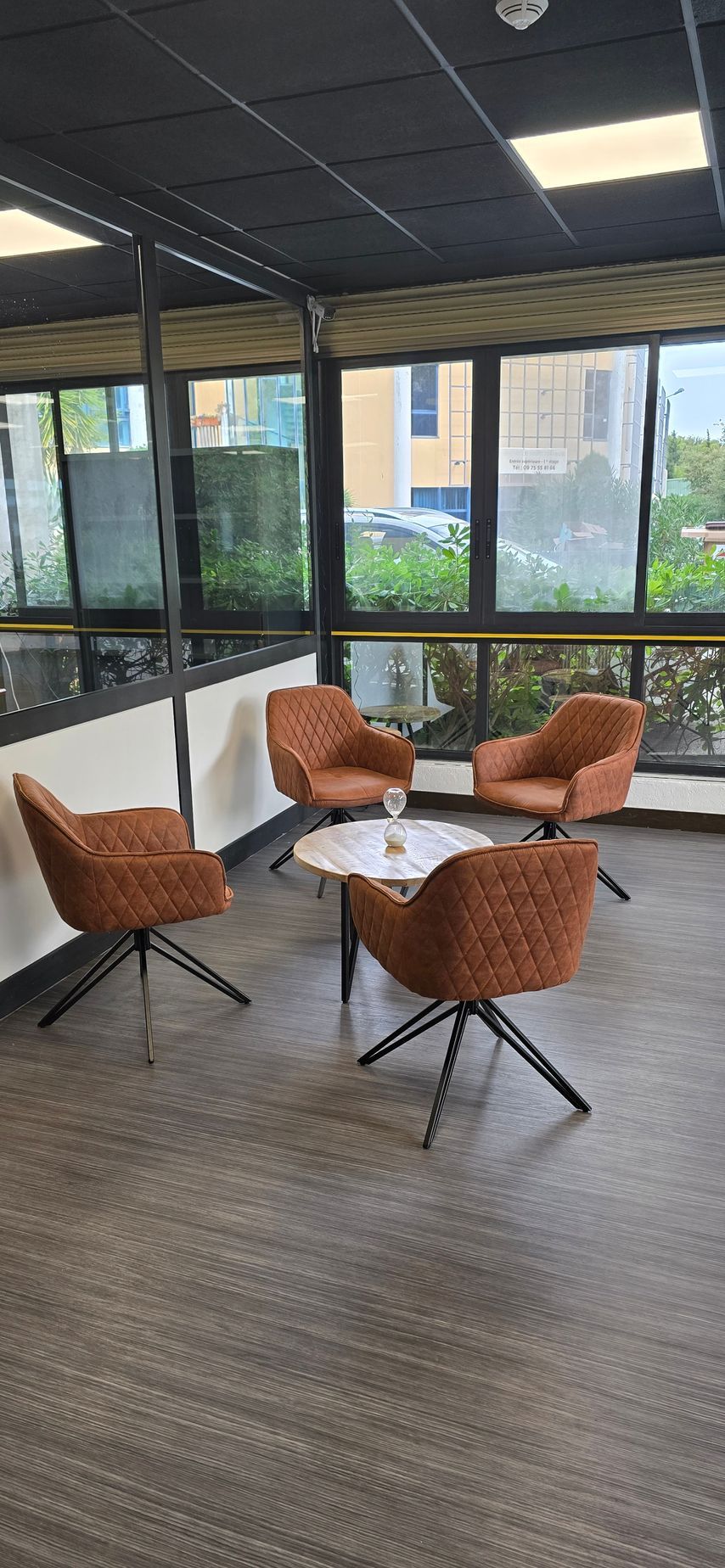 Quatre chaises marron autour d'une petite table dans une pièce avec de grandes fenêtres.