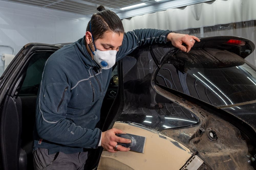 Carrossier ponçant une aile de voiture noire