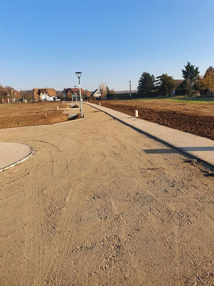 Un chemin de gravier serpente à travers un chantier dégagé, bordé de béton neuf.