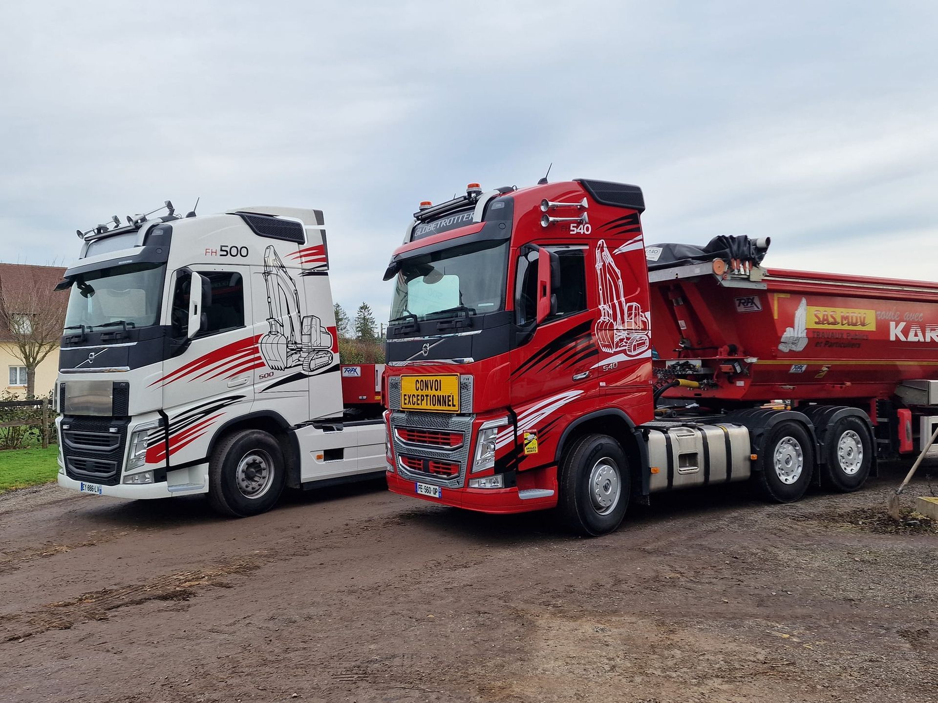 Deux semi-remorques garées côte à côte, l'une blanche et l'autre rouge, sur un terrain vague.