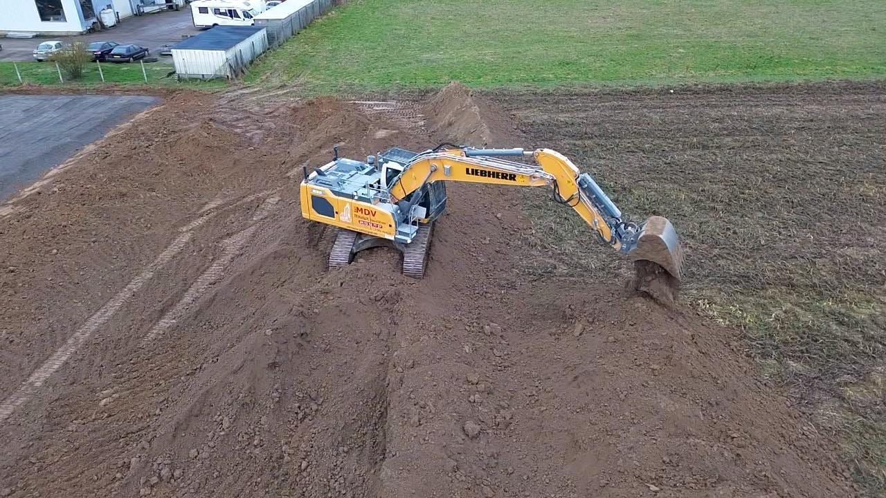 Vue aérienne d'une excavatrice jaune travaillant sur une parcelle de terre brune dans un champ ouvert.
