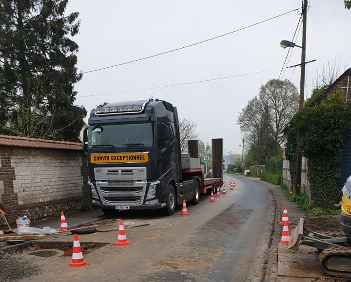 Un poids lourd sombre est stationné sur une route étroite balisée par des cônes de signalisation orange pendant des travaux de construction.