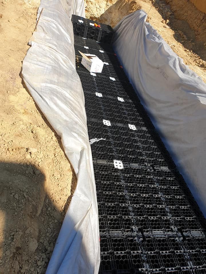 Un système de caissons d'infiltration modulaires en plastique noir pour le drainage, installé dans une tranchée tapissée d'un géotextile perméable blanc.